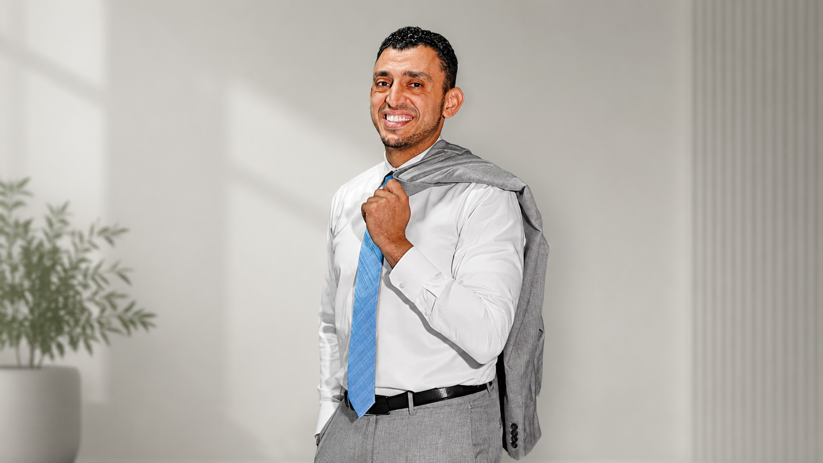 Ibrahim J. Awad in shirt and tie with his jacket slung over one shoulder, smiling to camera