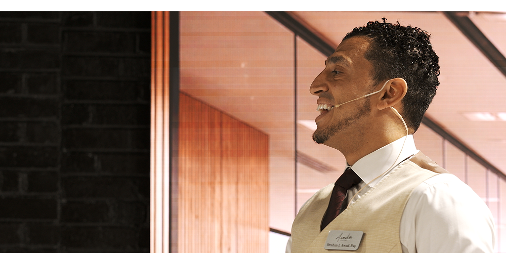 Ibrahim J. Awad in profile wearing a headset microphone, mid-talk