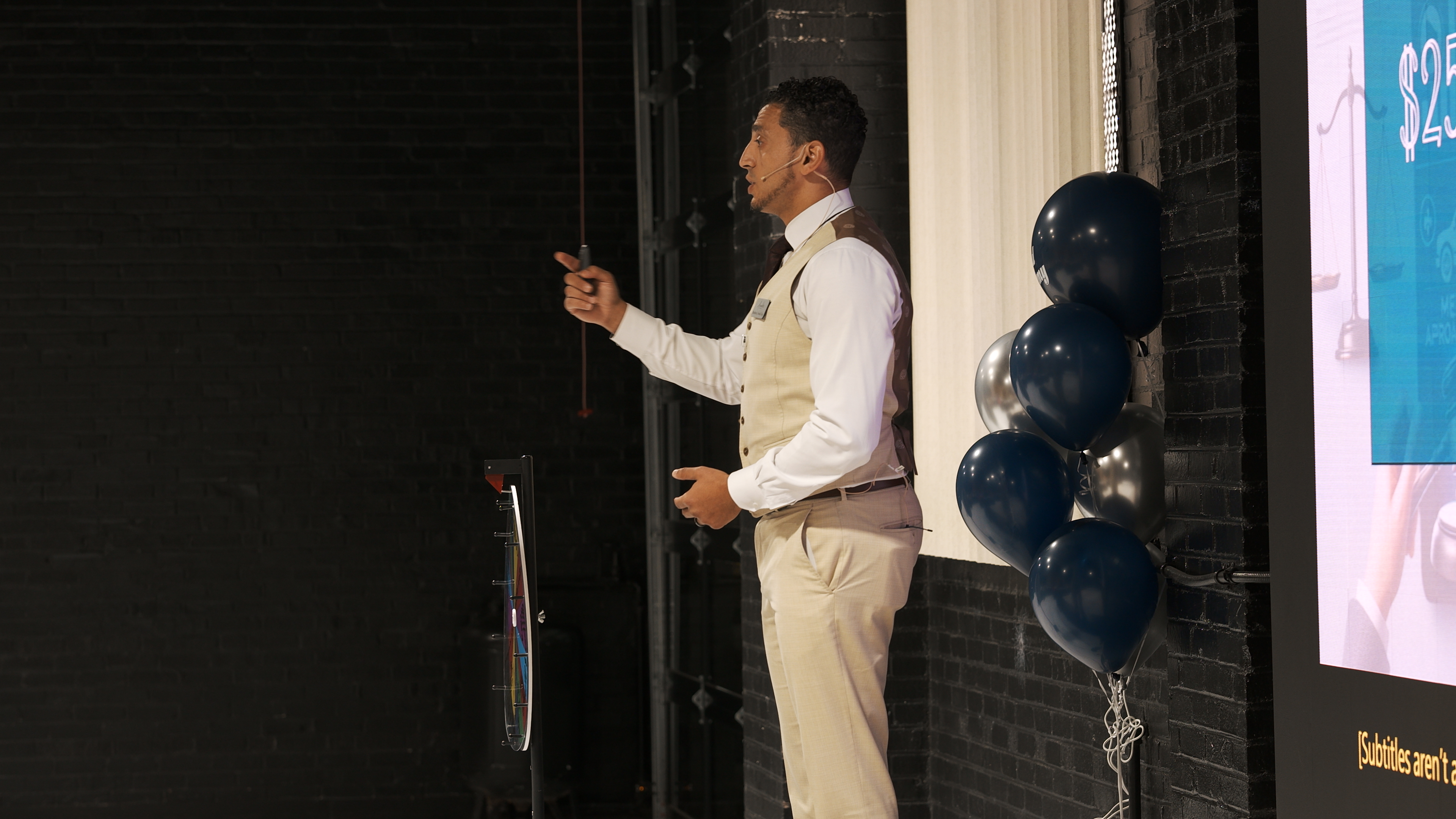 Ibrahim J. Awad presenting on stage with a headset mic, beside a presentation screen