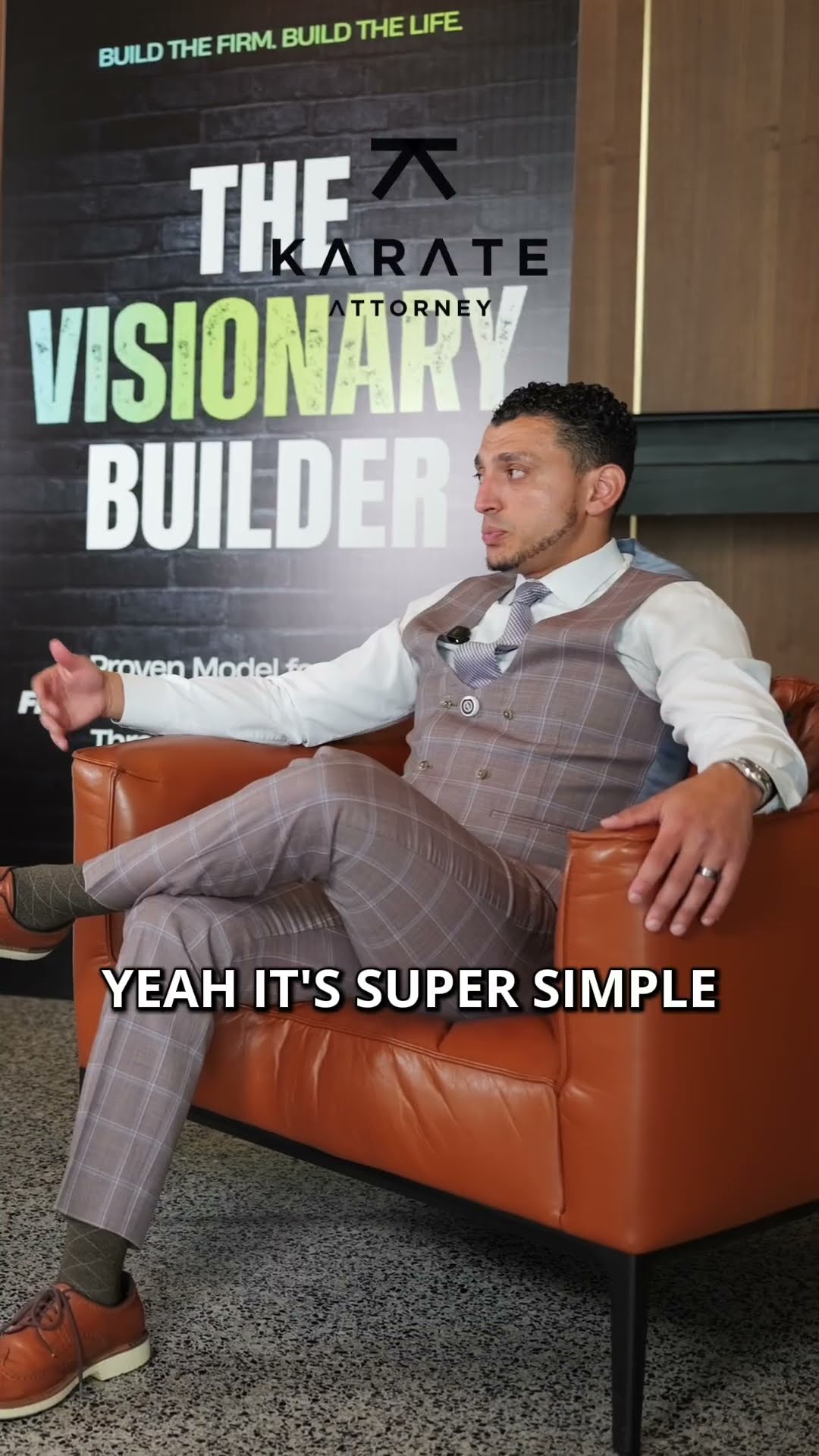 Ibrahim J. Awad seated in an orange armchair beside The Visionary Builder banner