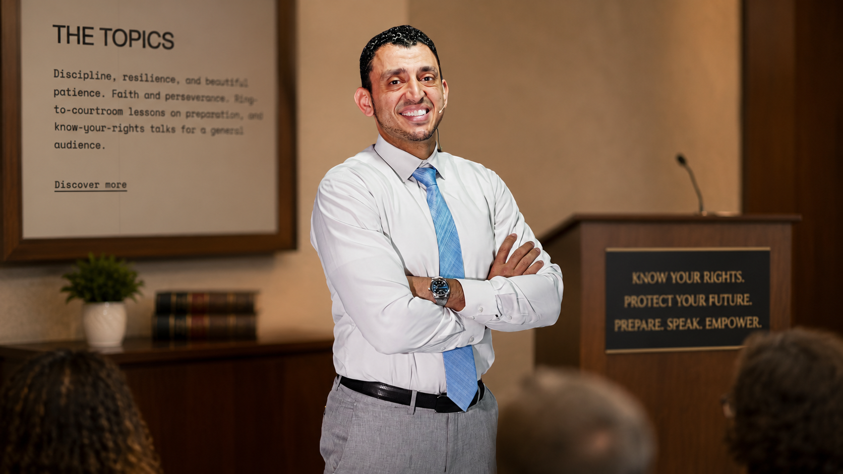 Ibrahim J. Awad addressing a seated audience, arms folded, beside a lectern